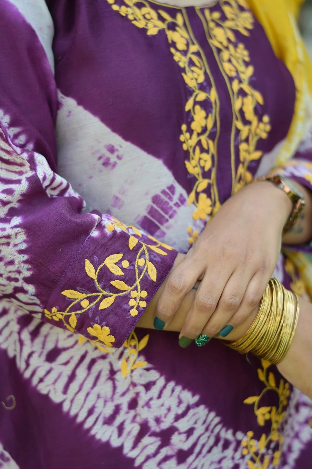 A woman wearing a vibrant purple and yellow kurta with tie-dye applique work and a matching dupatta, paired with yellow palazzo pants.