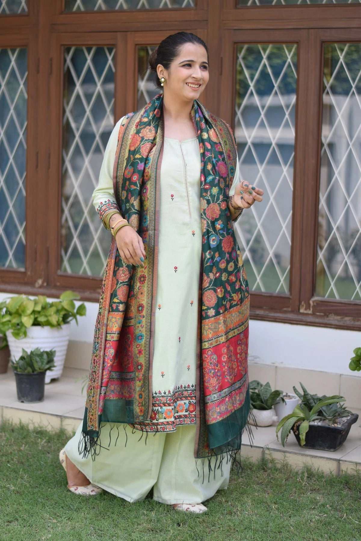 A woman wearing a stylish green silk jamawar dupatta with a green chanderi resham embroidered kurta and palazzo.