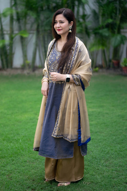 A woman wearing a beautiful blue kurta with golden zardozi work, paired with a stunning golden tissue dupatta and palazzo pants, creating a stunning traditional look.