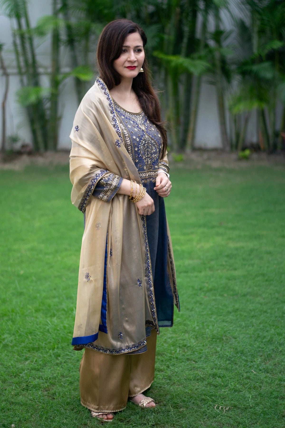 A stunning blue kurta with intricate gold embroidery paired with a matching golden tissue dupatta and palazzo pants, creating a stunning look for a woman.