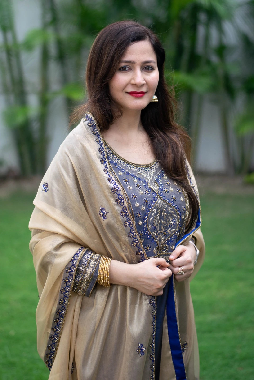 A woman wearing a blue kurta with intricate zardozi work and golden palazzo pants, holding a matching golden tissue dupatta draped over her arm.