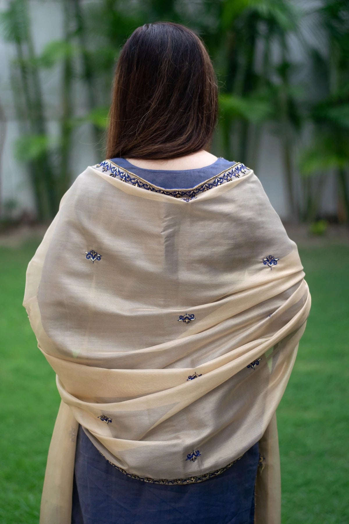 A woman wearing a blue kurta with intricate zardozi work and a matching golden tissue dupatta draped gracefully over her arms.