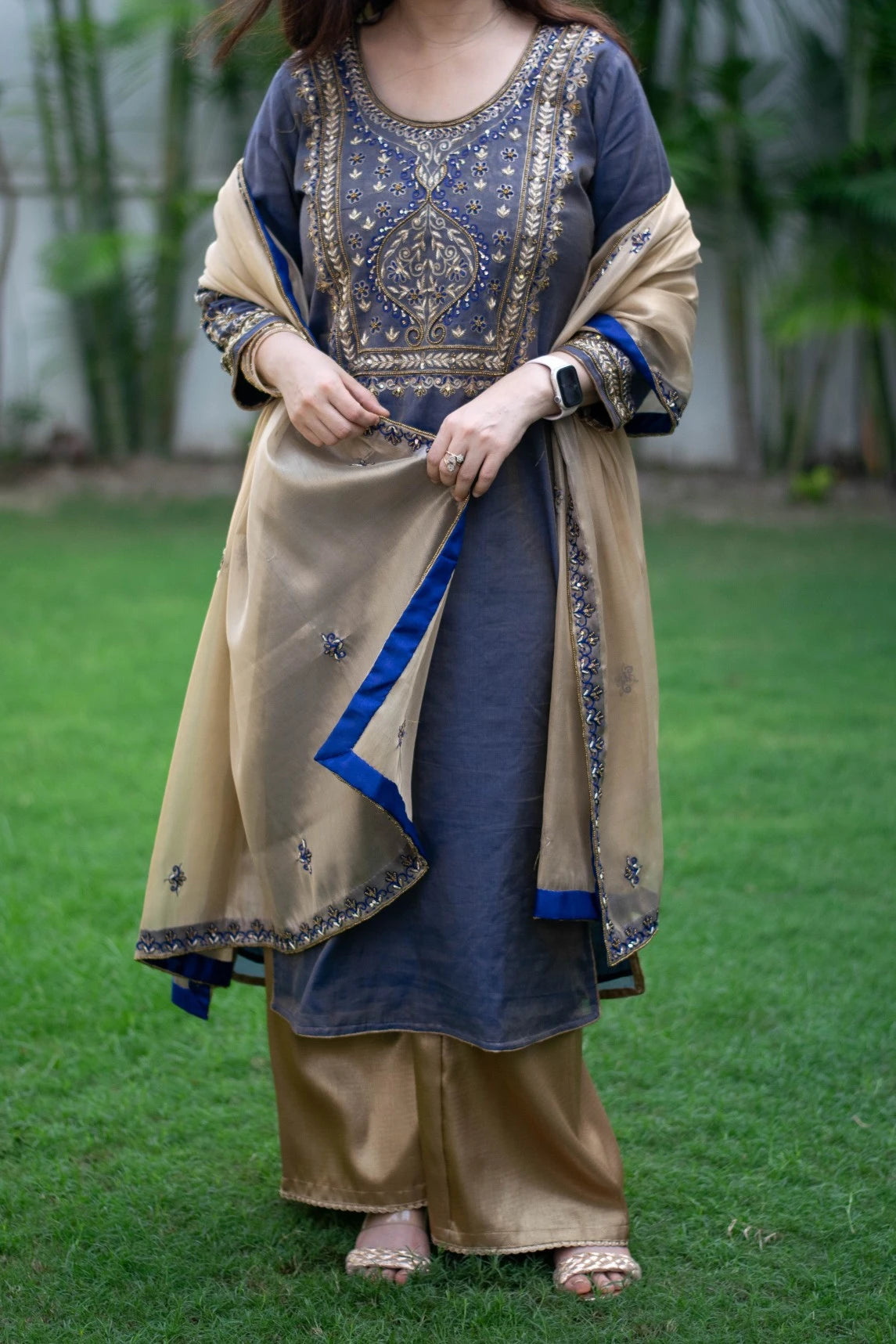 A woman wearing a blue kurta with gold zardozi work, paired with a gold tissue dupatta and palazzo pants, creating a stunning look.