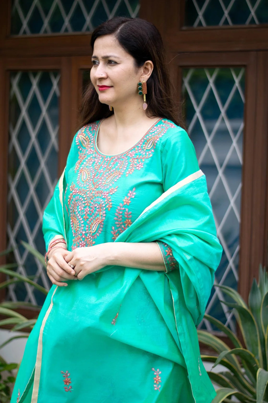 A woman dressed in a sea green zari kurta with an ornate neckline.