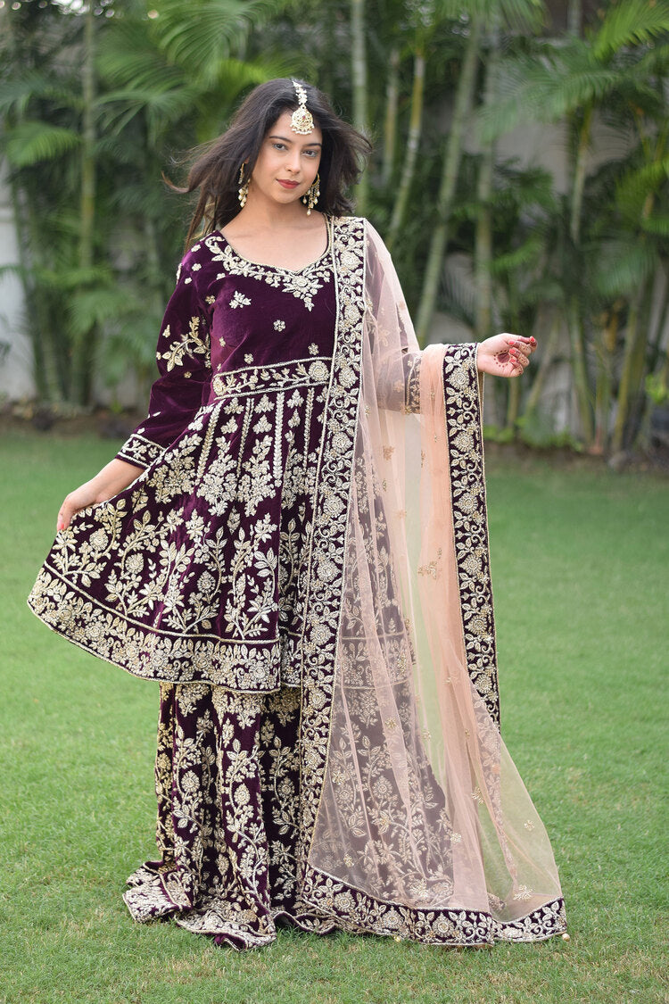 A woman wearing a traditional bridal outfit in rich wine velvet and detailed Zardozi embroidery.