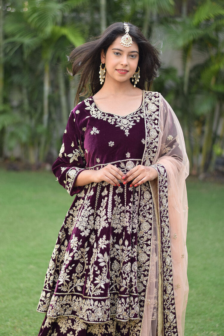 A bride dressed in a wine-colored velvet lehenga set with intricate Zardozi work.