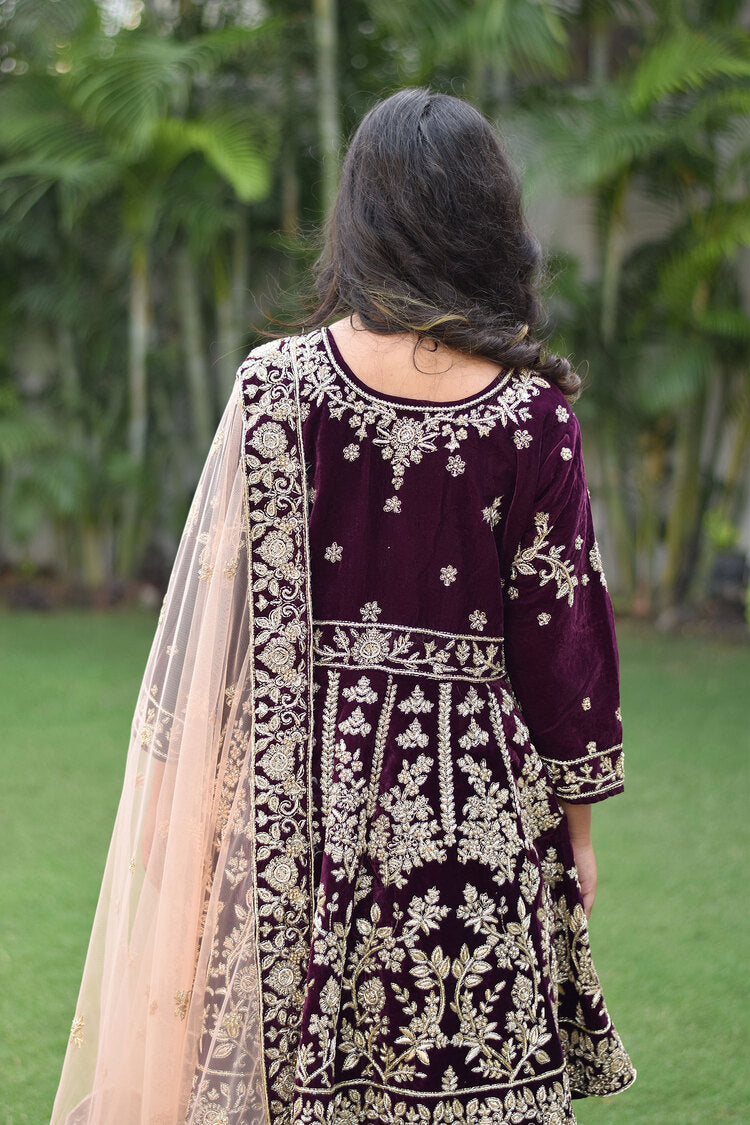 A beautiful bride in a wine velvet lehenga set featuring detailed Zardozi work and rich gold embroidery.