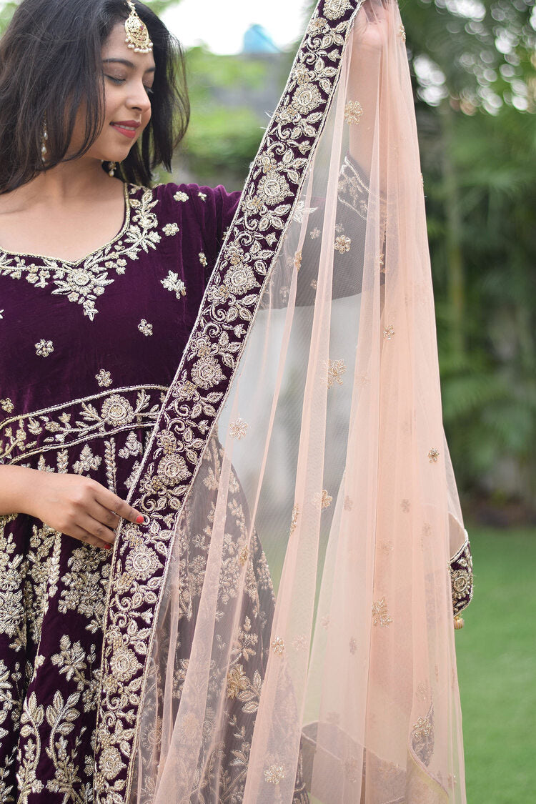 A beautiful bride in a wine velvet lehenga set with ornate Zardozi work, a perfect choice for a grand wedding.