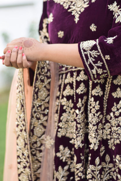 An elegant woman dressed in a wine-colored velvet lehenga set with intricate Zardozi work.