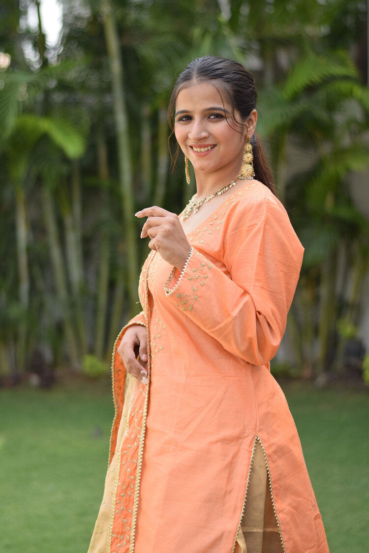 A traditional Indian outfit consisting of a Peach Kamkhab Farshi Gharara, Peach Chanderi Kurta & Golden Dupatta with Tissue Applique Work