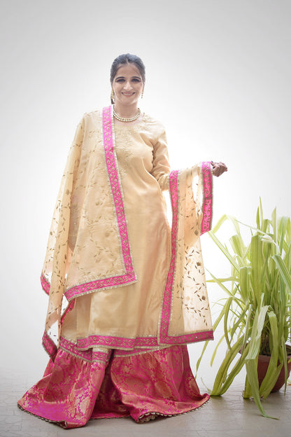 A lady dressed in a gorgeous traditional outfit consisting of a Magenta Kamkhab Farshi Gharara and Golden Chanderi Kurta & Dupatta with Tissue Applique Work.