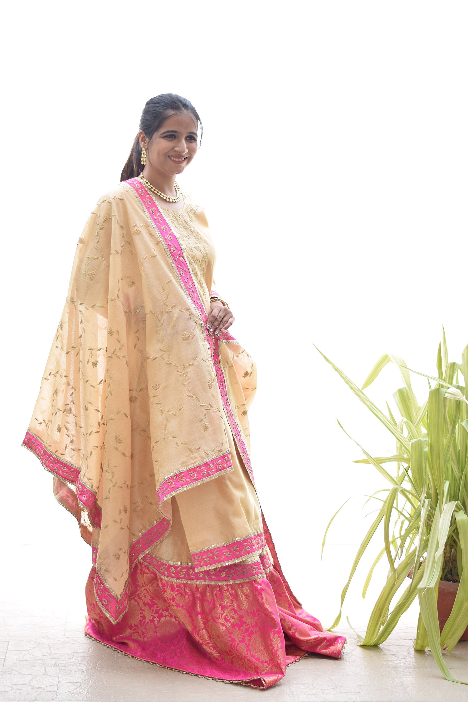 A fashion-conscious woman donning a Magenta Kamkhab Farshi Gharara, Golden Chanderi Kurta & Dupatta with Tissue Applique Work.