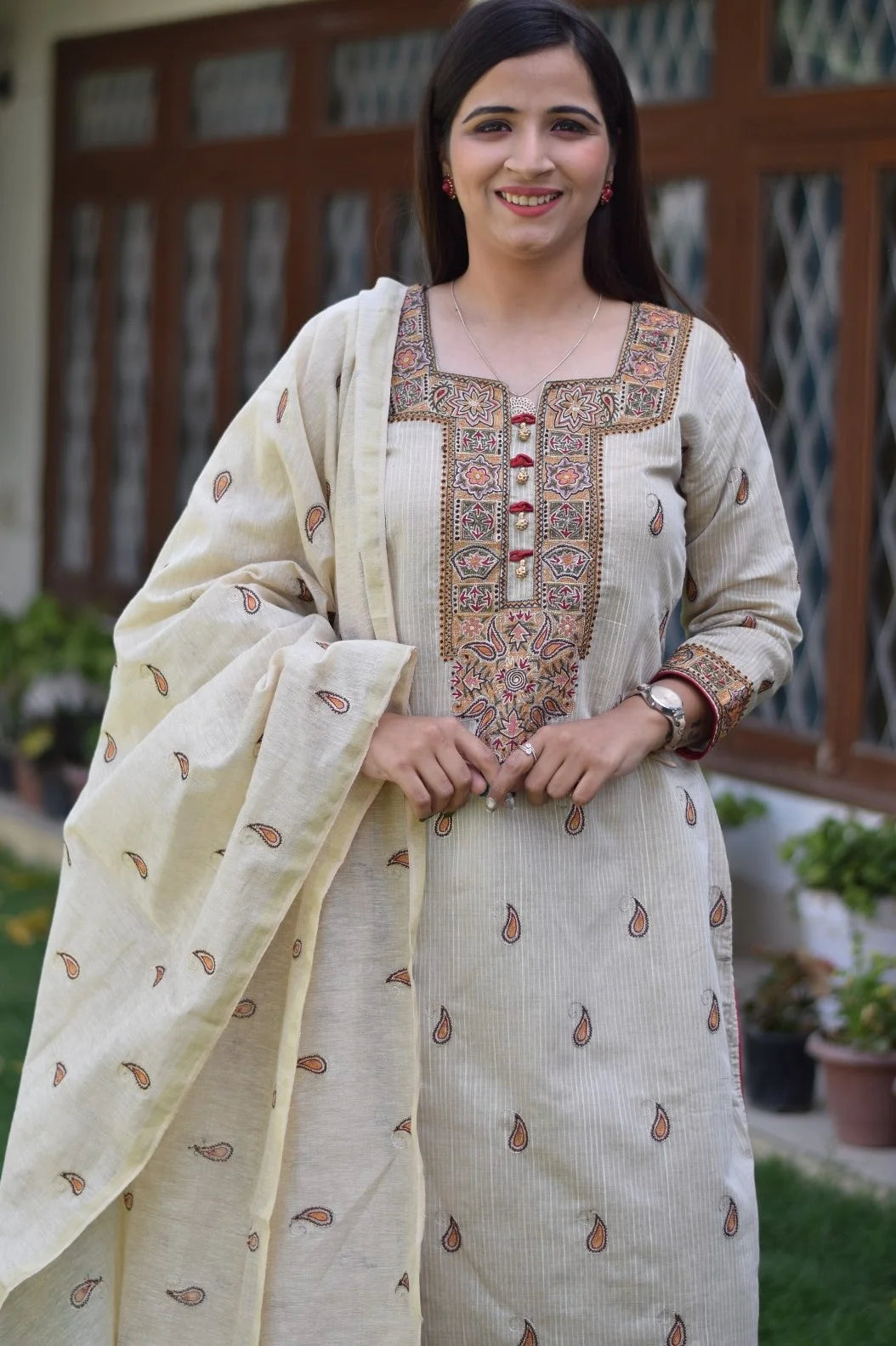 A woman wearing a beige chanderi kurta with intricate hand embroidery paired with beige trousers and dupatta.