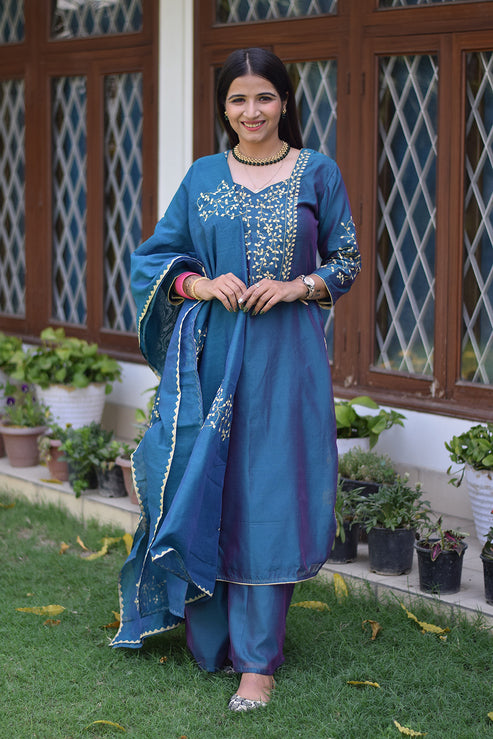A solo Indian woman dressed in a blue suit with intricate applique work.