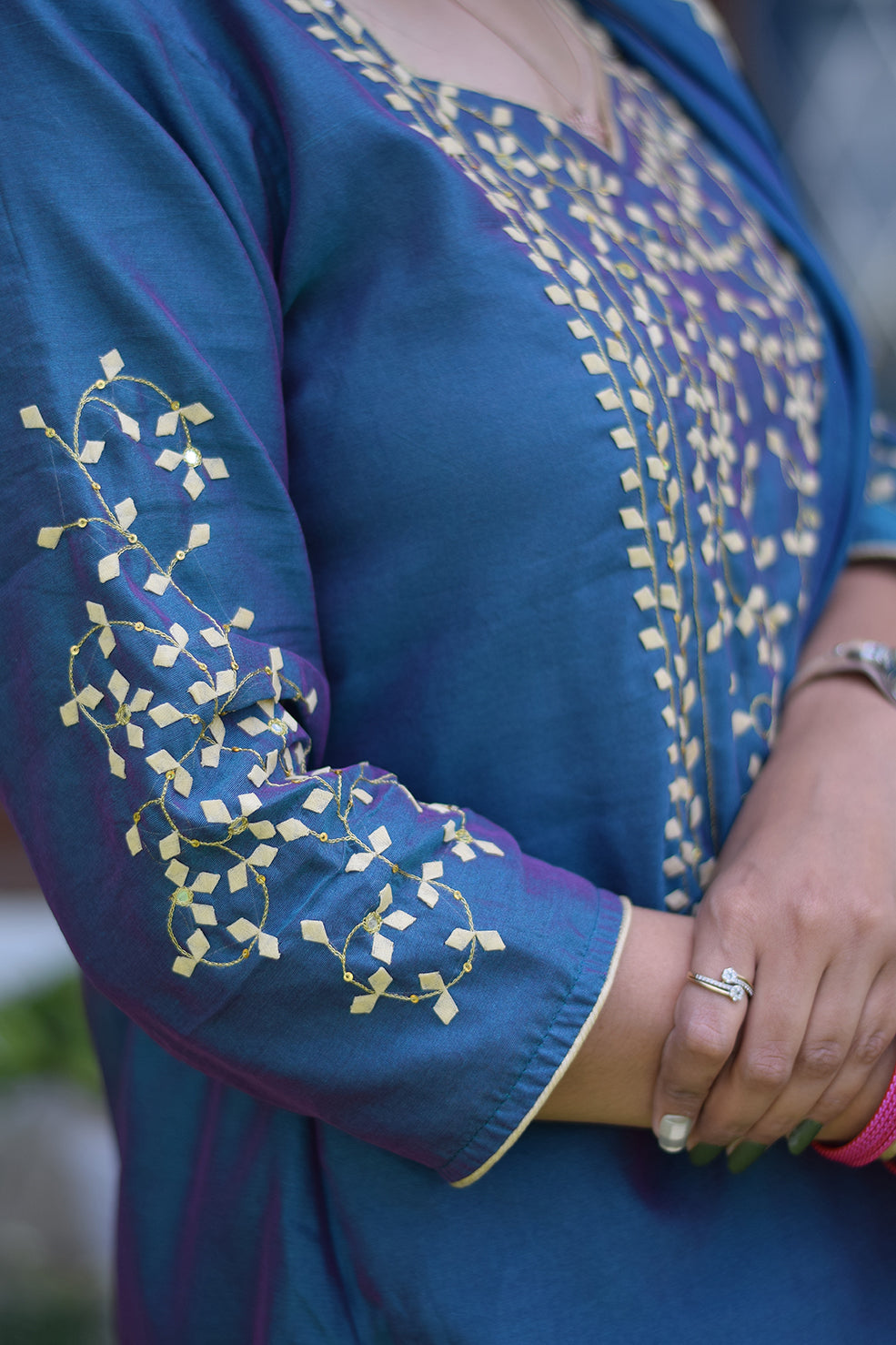 An Indian lady posing in a blue suit embellished with intricate applique work.