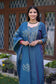 A young Indian woman standing confidently in a blue applique work suit.