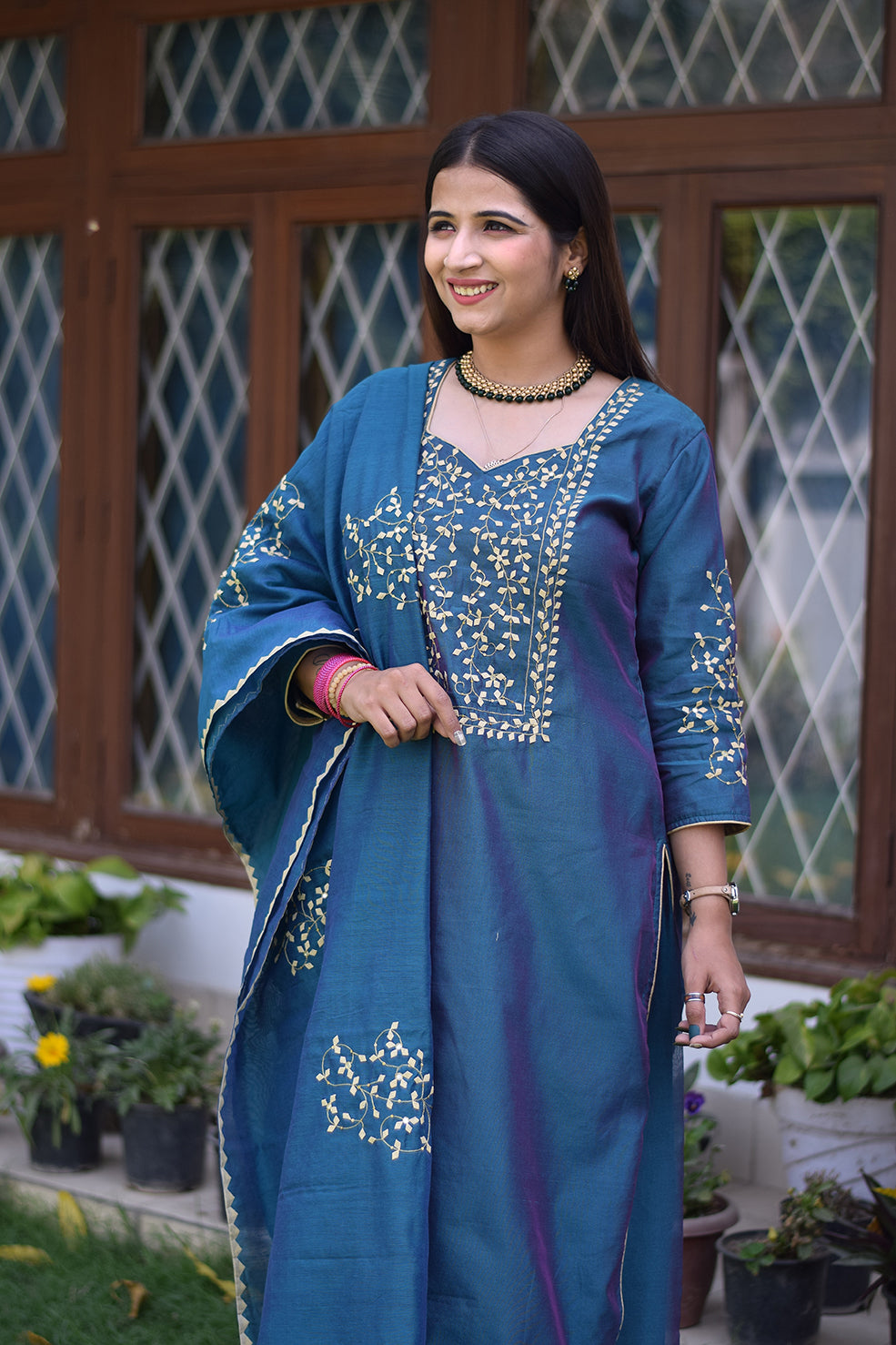 A solo female in a gorgeous blue applique work suit standing against a plain background.