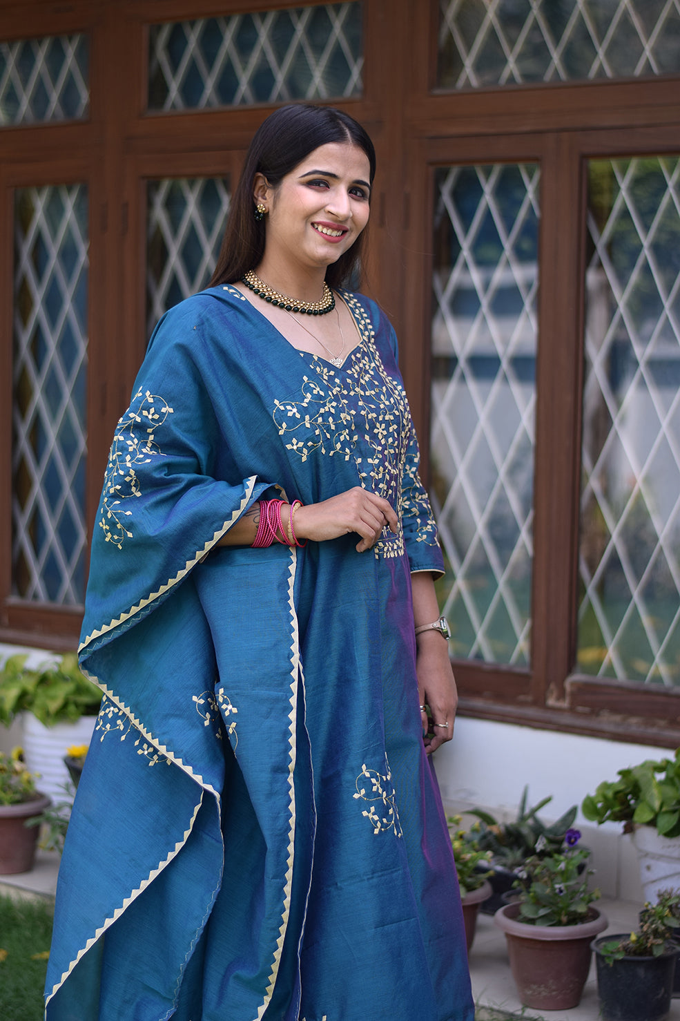 A beautifully dressed Indian woman in a blue applique work suit looking directly at the camera.