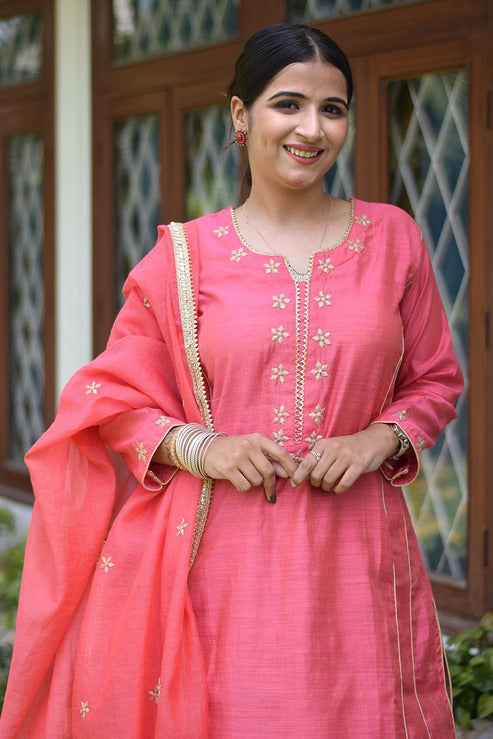 A smiling Indian woman wearing a jute kurta and standing against a white wall.