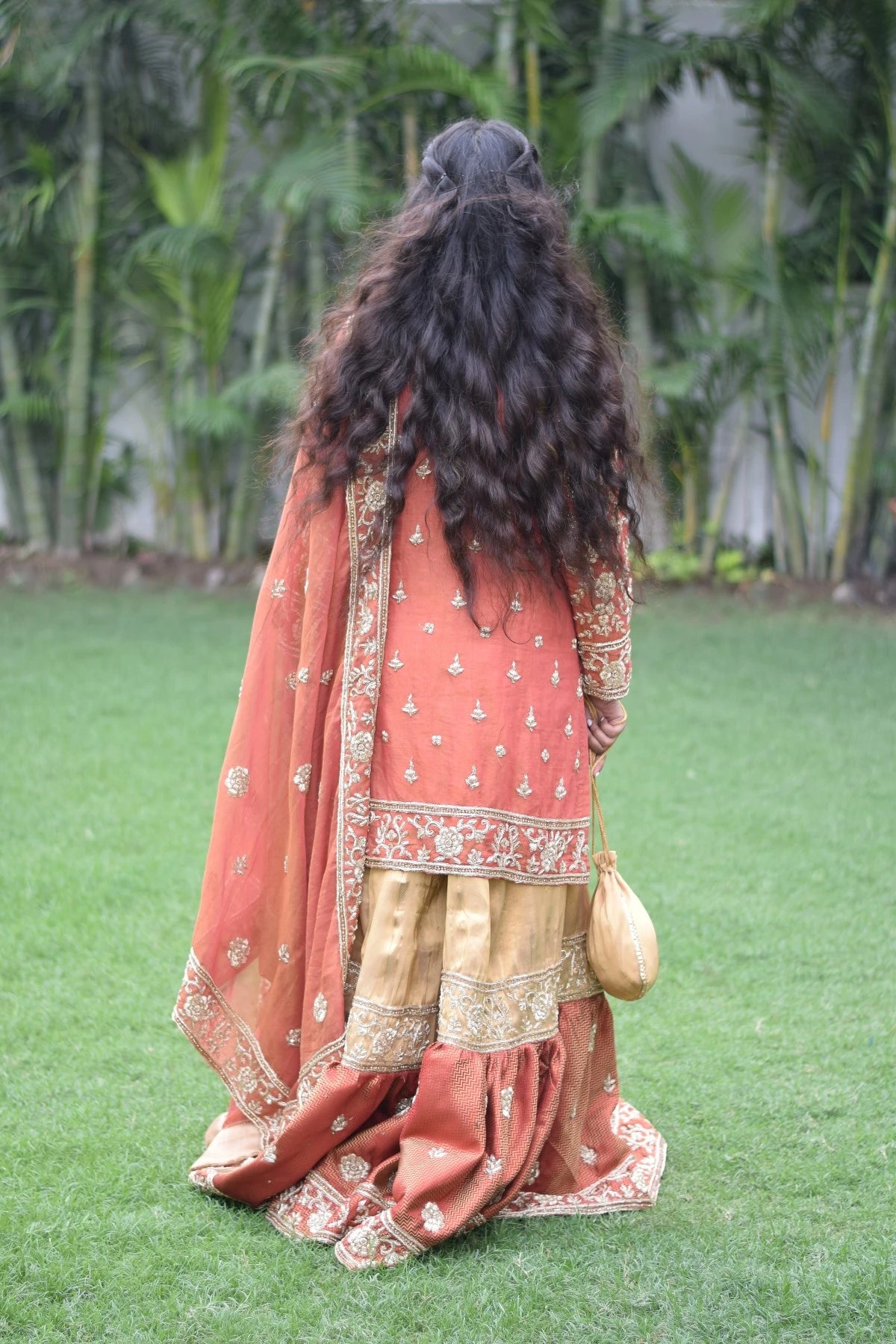 A graceful woman wearing a regal farshi gharara in golden rust.
