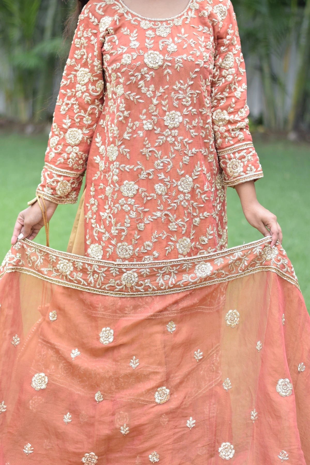 A woman looking glamorous in a golden rust farshi gharara with exquisite work.