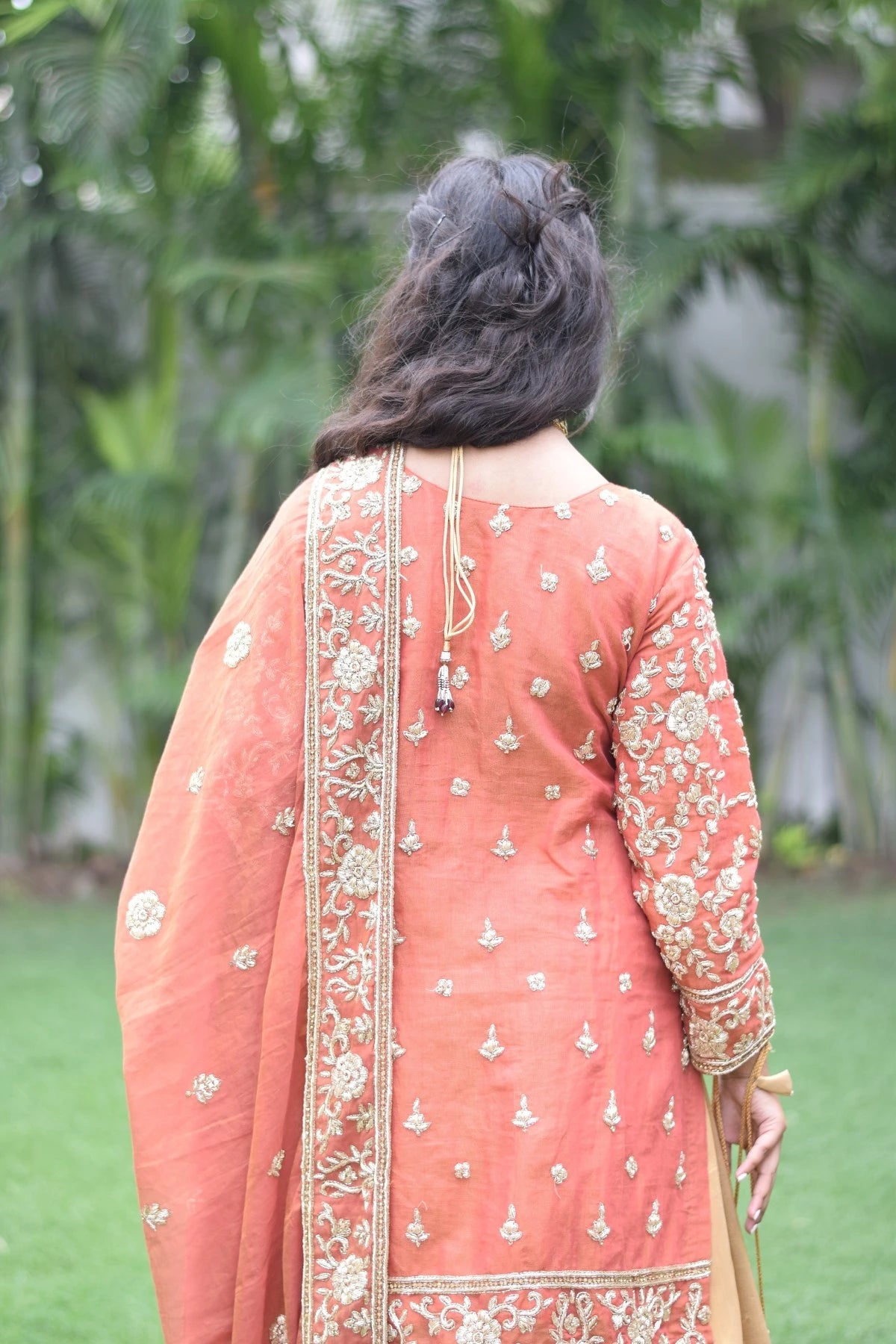 A lady dressed in a classic farshi gharara with golden rust detailing.
