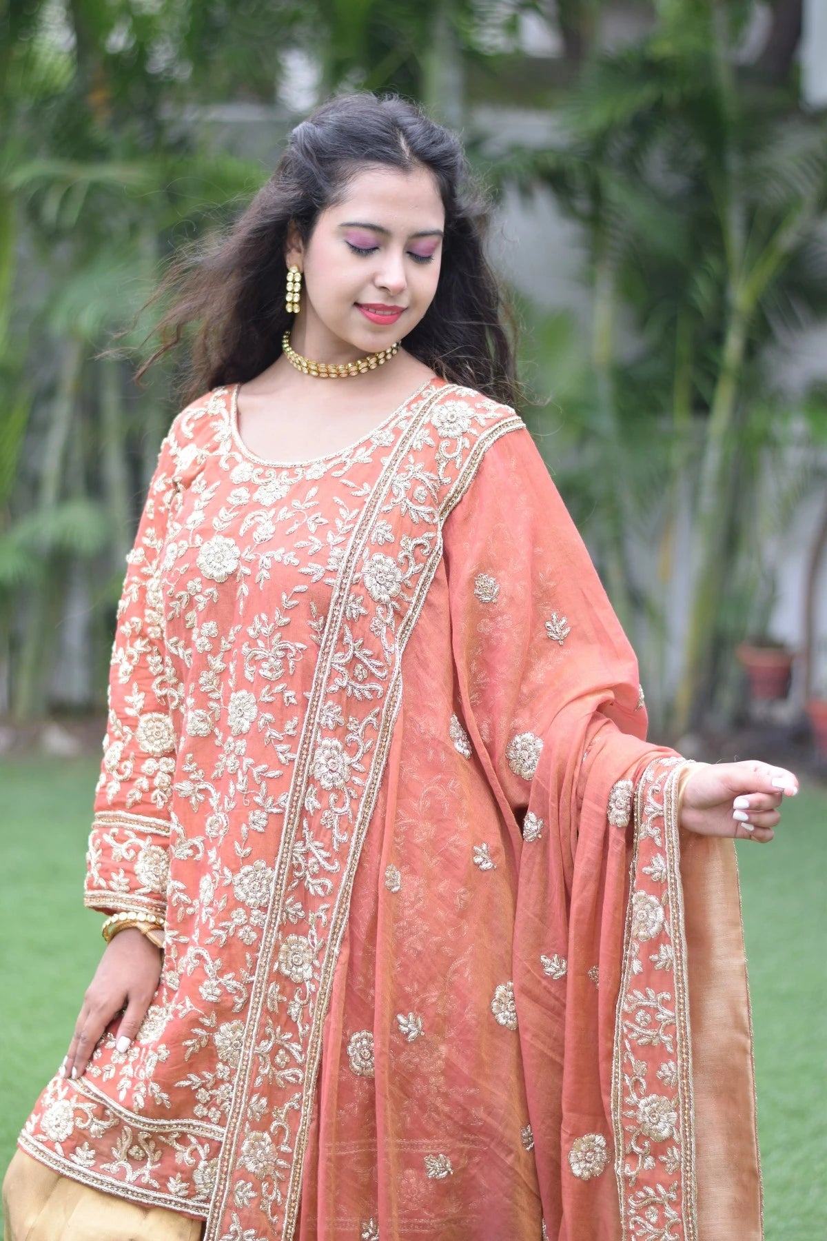 A lady in a traditional farshi gharara featuring golden rust hues.