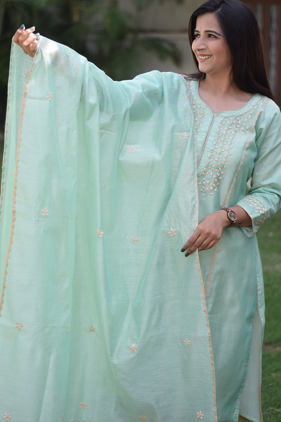 A lady wearing a sea green Aari work kurta with traditional patterns