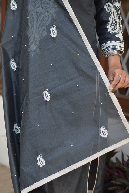 A graceful Indian woman dressed in a grey kurta with a dupatta.