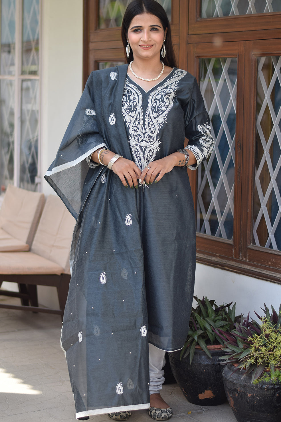 An Indian lady dressed in a grey kurta and dupatta set.