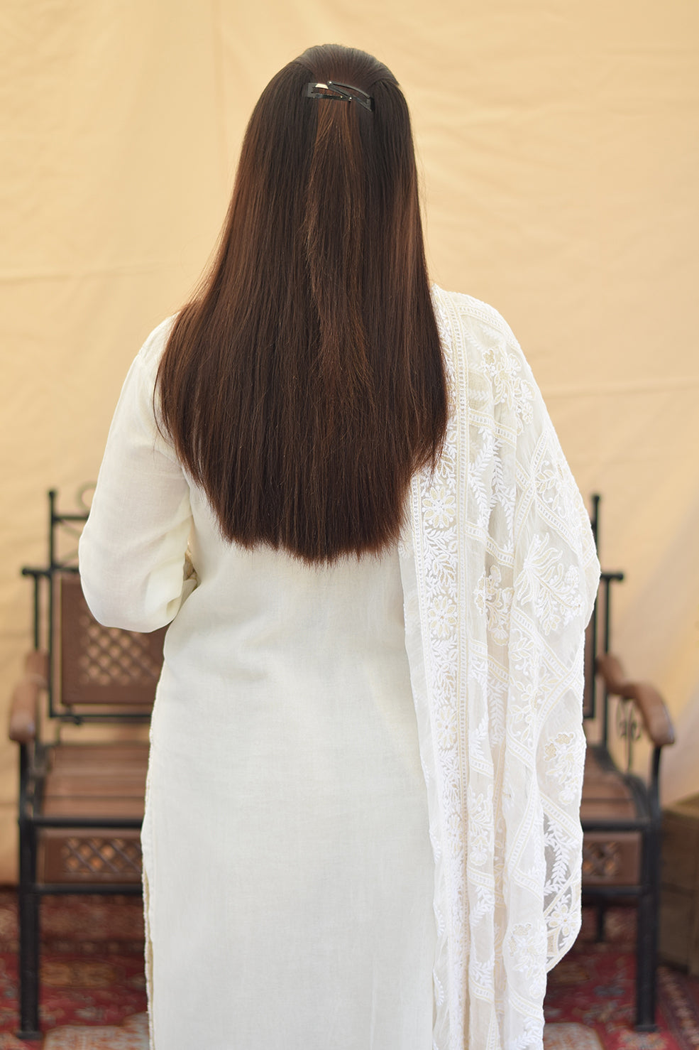 A woman's back in a white georgette kurta, showcasing the delicate chikankari embroidery on the upper back and the elegant drape of the fabric.