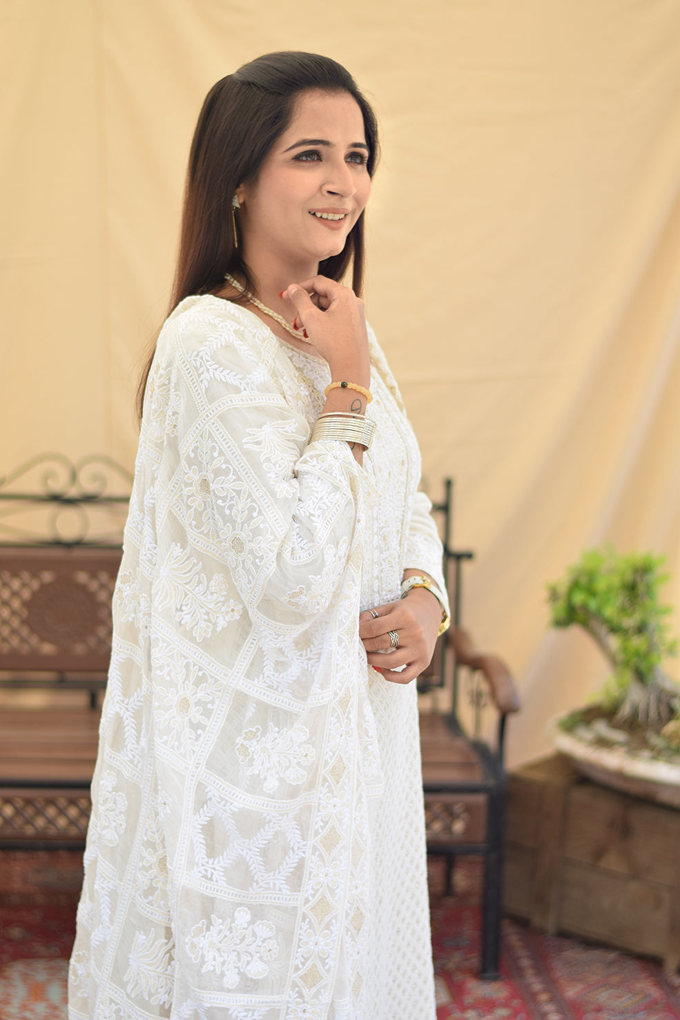 A woman posing in profile, showcasing the delicate chikankari embroidery and flowing silhouette of her white georgette kurta and dupatta, paired with golden trousers.