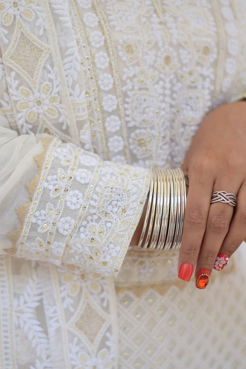 Close-up of a woman's hands adorned with delicate chikankari embroidery on the sleeves of her white georgette kurta.