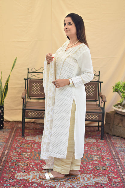 A woman in a side pose, wearing a white georgette chikankari kurta with intricate kikri and kamdani embroidery, paired with a matching dupatta and golden trousers.