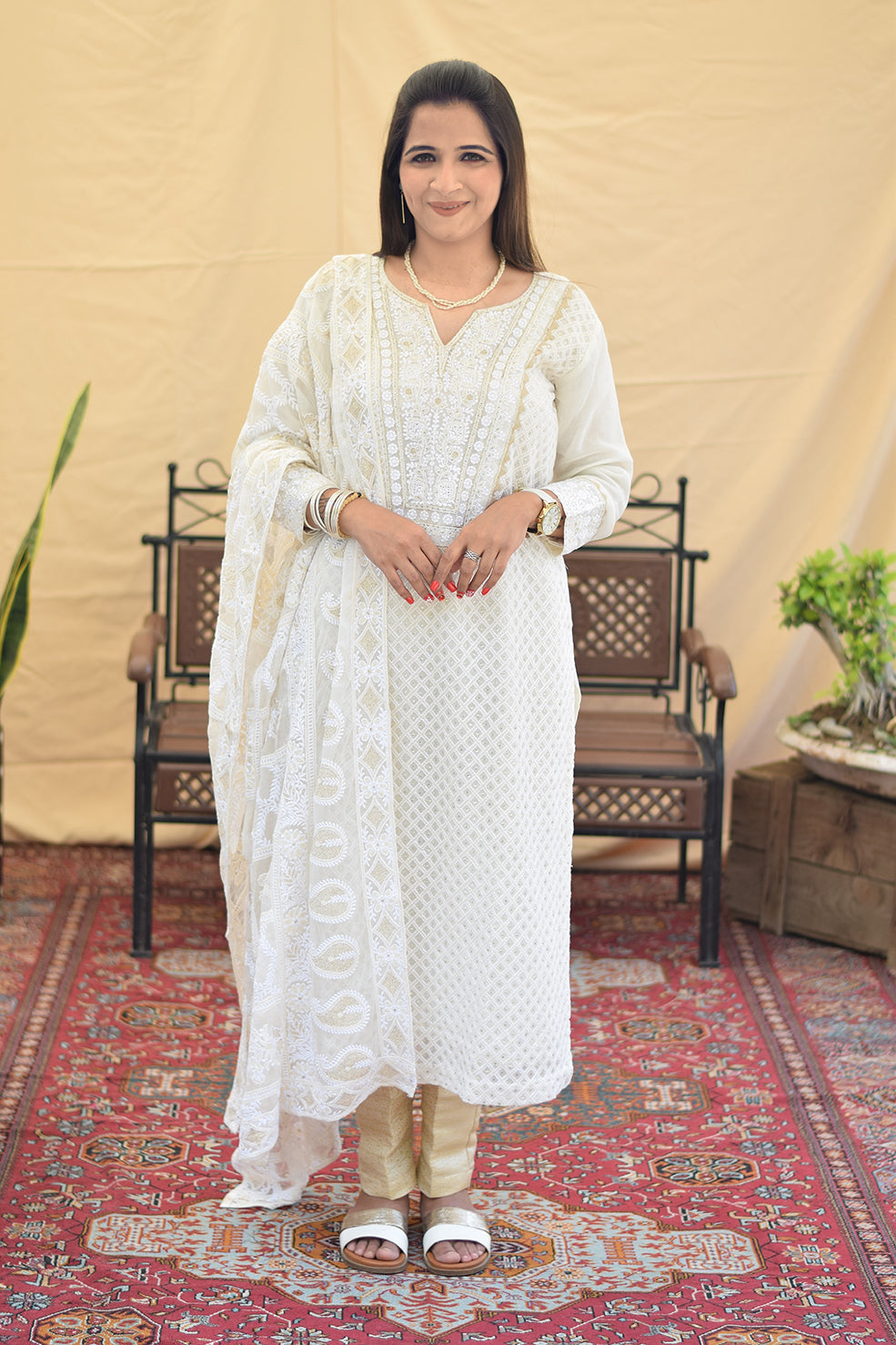 A woman posing in a white georgette chikankari kurta with intricate kikri and kamdani embroidery, paired with a matching dupatta and golden trousers.