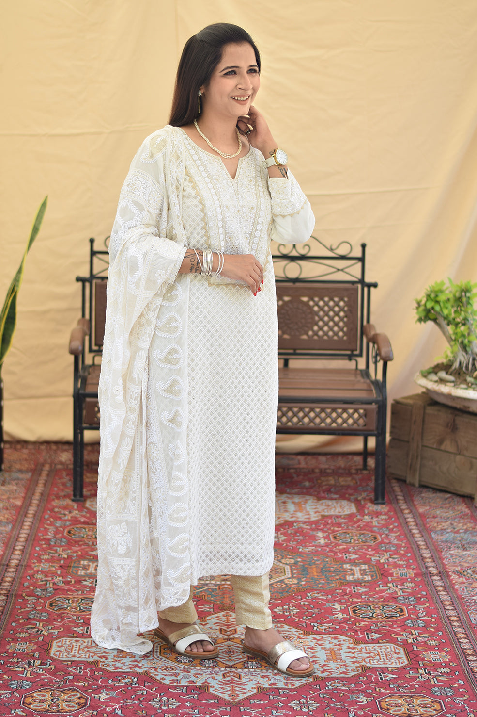 A woman gracefully poses in a side profile, showcasing the delicate chikankari embroidery and flowing silhouette of her white georgette kurta and dupatta