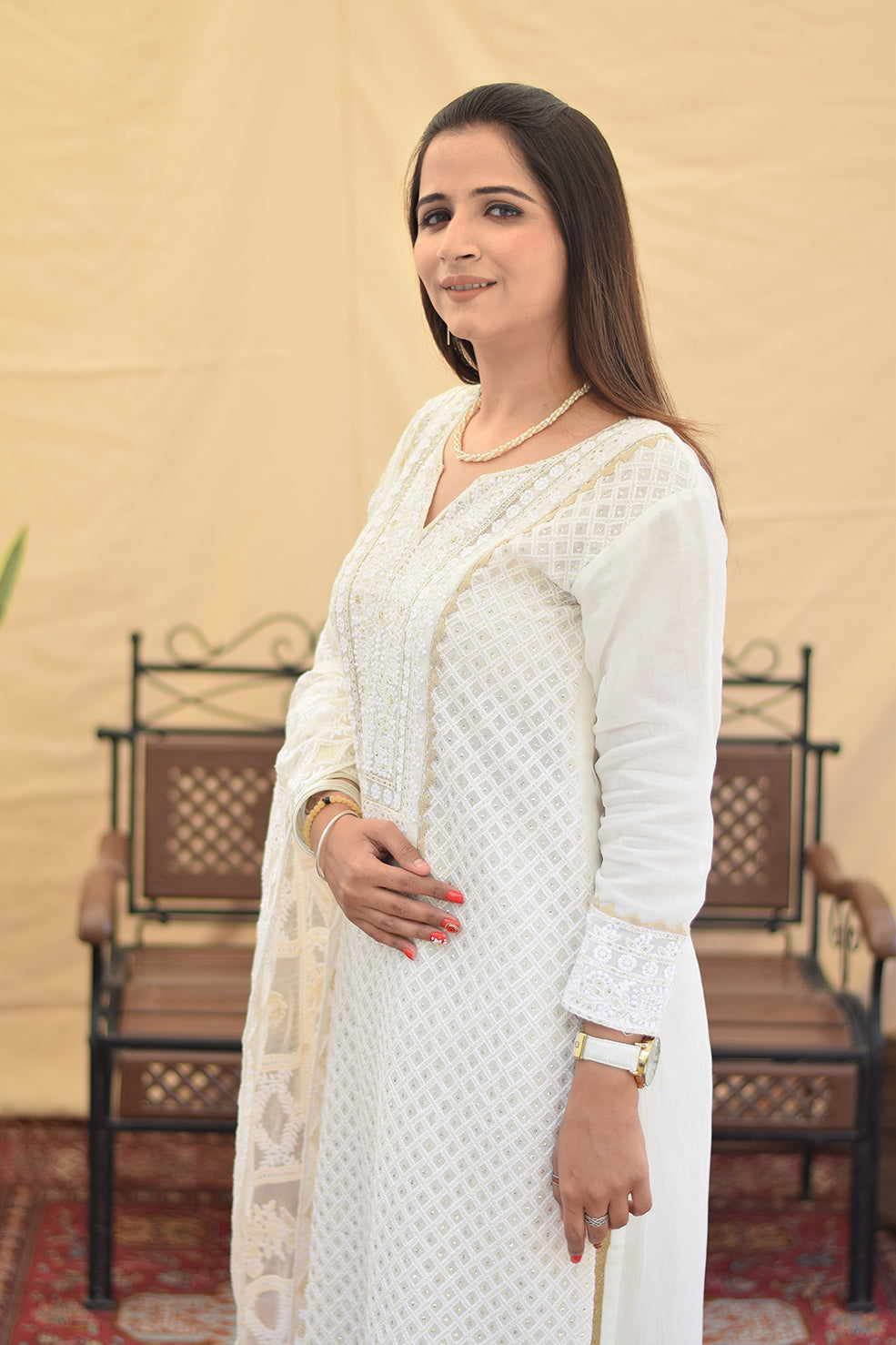 A woman posing in profile, showcasing the delicate chikankari embroidery and flowing silhouette of her white georgette kurta and dupatta.