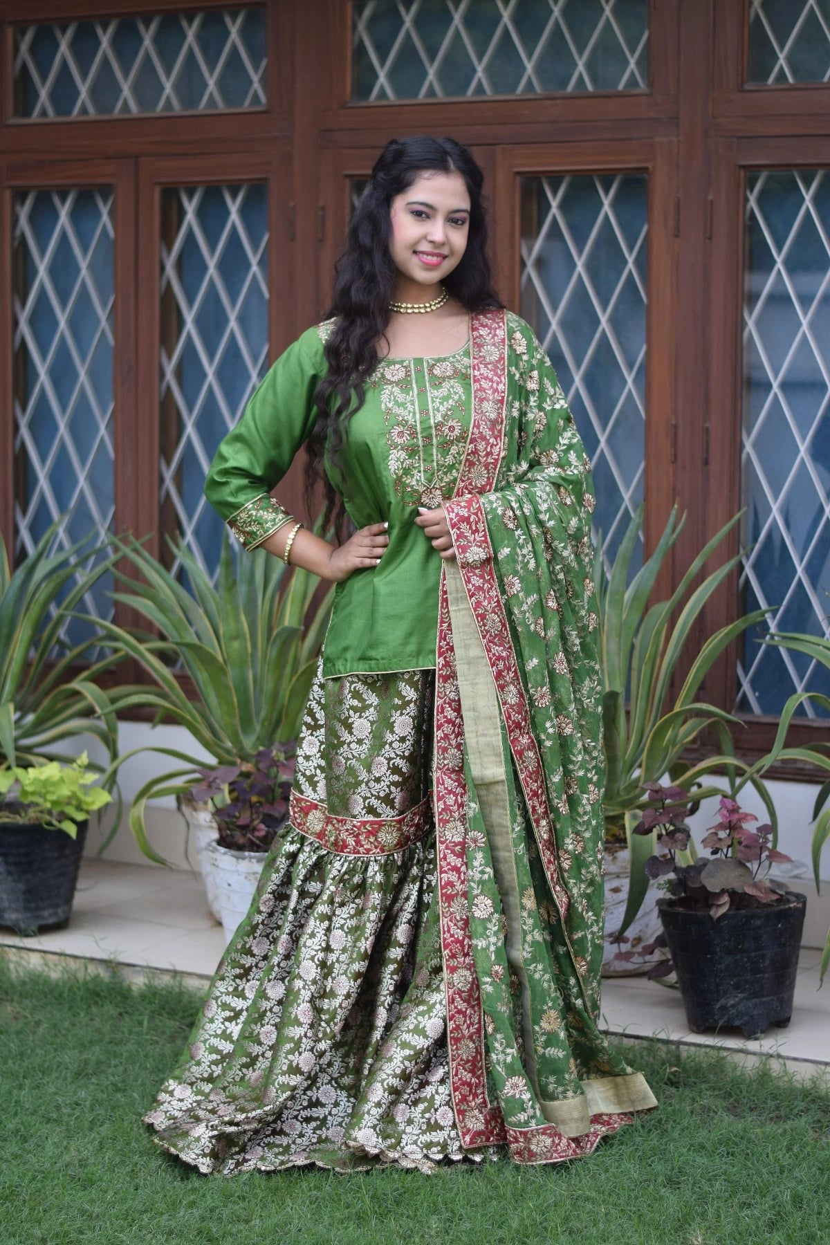 A woman wearing an exquisite green kamkhab zardozi embroidered wedding gharara suit.