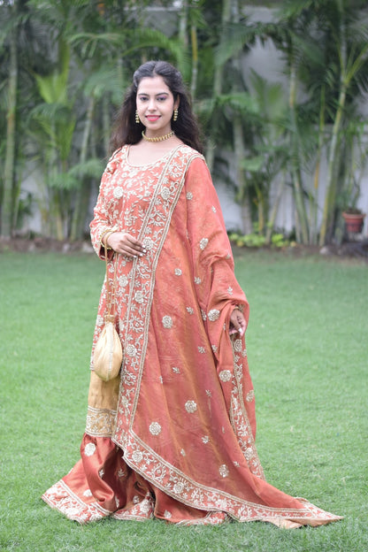 A woman donning a farshi gharara with intricate golden rust embroidery.