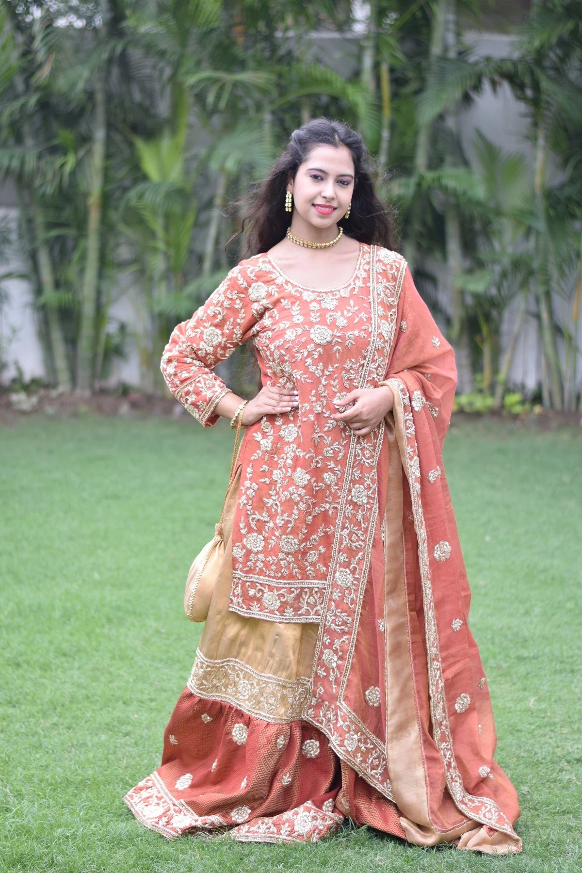 An elegant lady in a traditional golden rust farshi gharara.