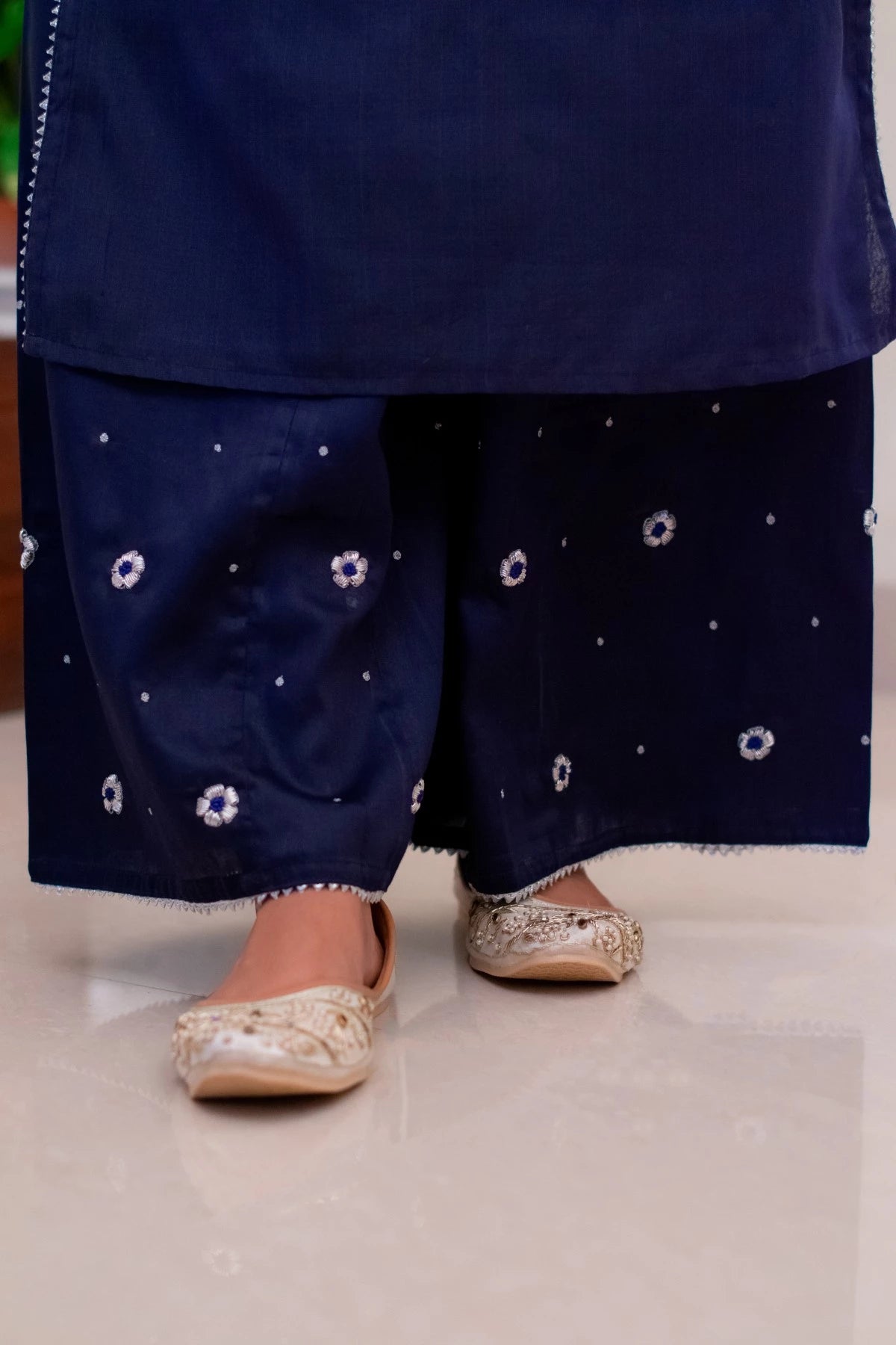 A woman in a blue kurta and a plain blue dupatta, carrying a basket of flowers as part of a traditional Indian ritual.