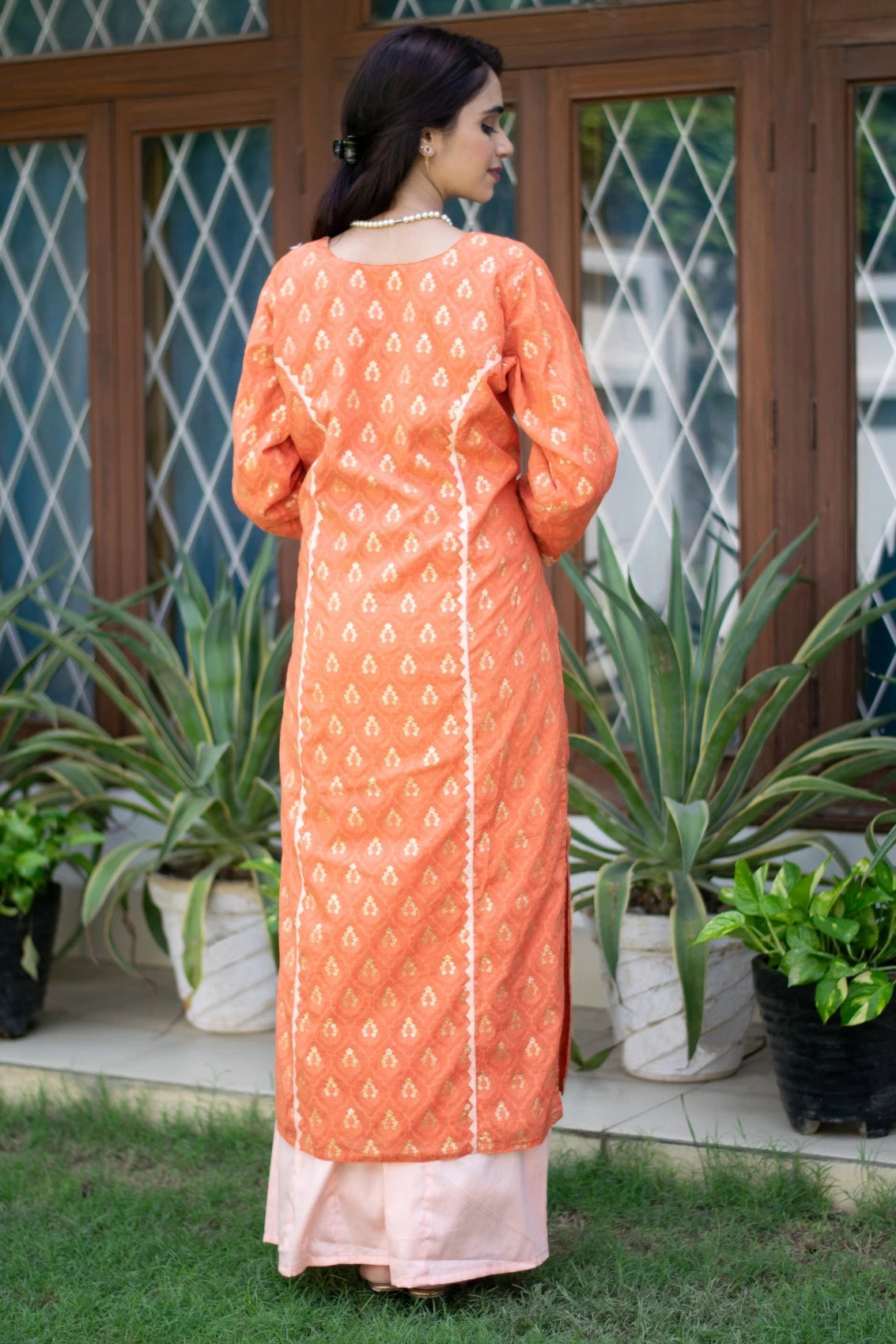 A woman posing confidently in a fashionable orange silk kurta and trousers