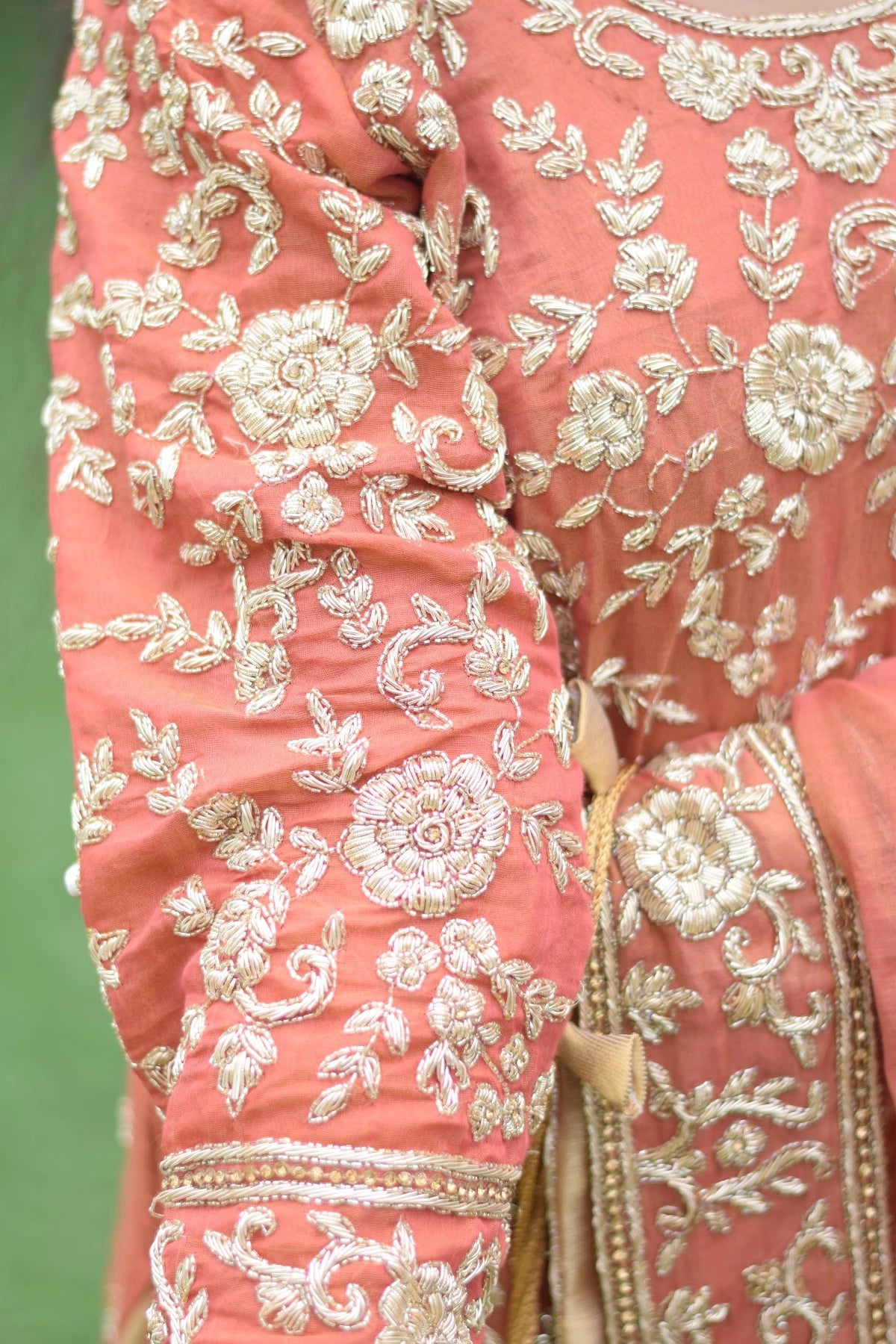 A woman in a magnificent golden rust farshi gharara with intricate patterns.
