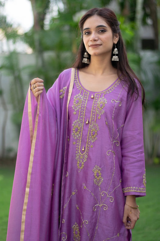 A woman wearing a purple lilac cut dana kurta with matching trousers stands against a plain white wall.